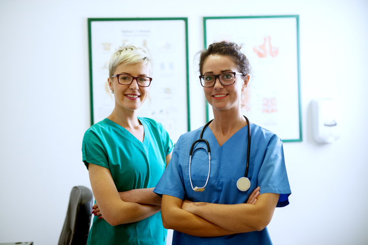 Two confident nurses standing with arms crossed in a modern medical office, representing nursing career growth, staffing goals, and professional advancement in today’s healthcare workforce.