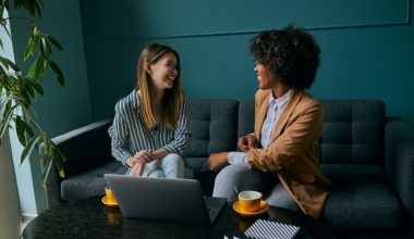 Two young businesswomen are networking in a quiet coffee shop, collaborating over a laptop in a calm, introvert‑friendly setting that supports building referrals without small talk.