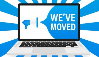 Illustration of a laptop displaying a blue megaphone and the text “WE’VE MOVED,” with blue and white radial rays emanating in the background.